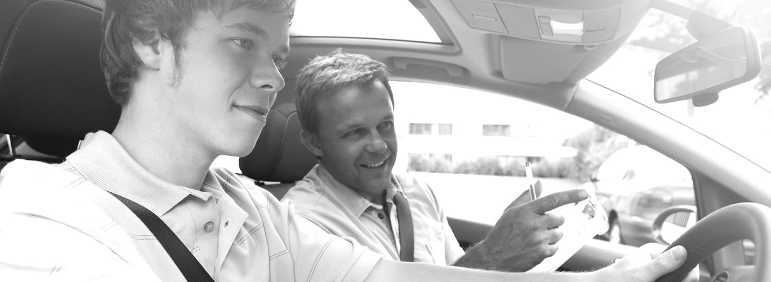 Driver instructor in the front seat of the car talking to a student driver in the passenger seat